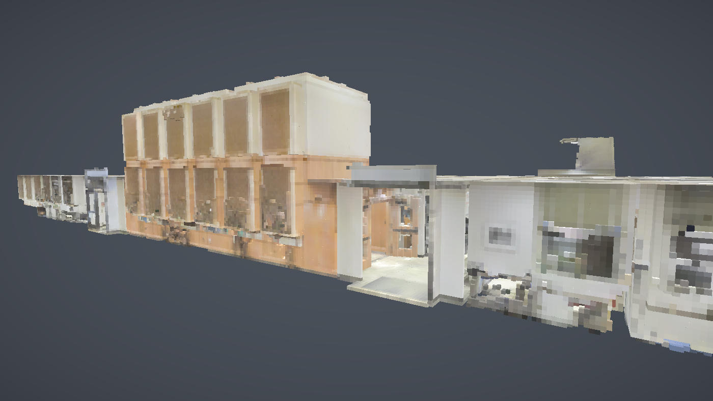 A wing of the voxelised office floor seen in cutaway at eye level, its rooms side by side in the scan's own colours